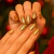 Unhas com esmalte dourado metálico brilhante aplicado, em fundo com decoração natalina desfocada