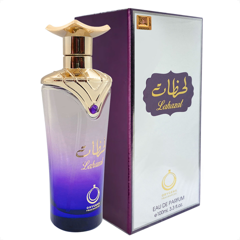 Perfume árabe Orygens Fragrances Lahazat EDP 100ml em frasco violeta com detalhes dourados ao lado da embalagem branca com detalhes roxos e dourados