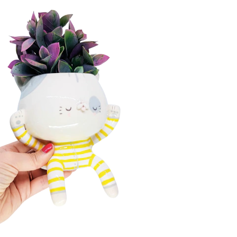 Maceta en forma de gatito sentado con pijama, decorada con plantas verdes y moradas.
