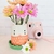 Maceta decorativa en forma de gatito mediano con platito verde y cuerpo en tonos blanco y rosa.