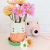 Maceta decorativa en forma de gatito mediano con platito verde y cuerpo en tonos blanco y rosa.