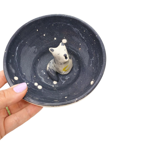 Cuenco de cerámica oscuro con un lobo decorativo en el centro, sostenido por una mano.