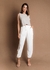 Modelo vestindo calça alfaiataria off white, combinada com uma blusa sem mangas, em fundo marrom.