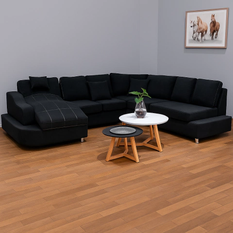 Diván esquinero tapizado en negro con cojines, acompañado de mesas de centro en un ambiente moderno. Conseguilo en Gamma Hogar.