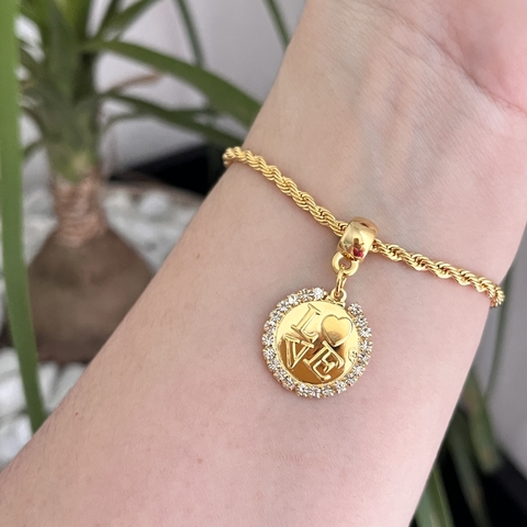 Pulseira folheada em dourado com pingente em formato de círculo, decorado com cristais e a palavra "LOVE".
