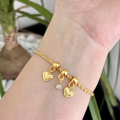 Pulseira dourada com três corações em pingentes e um detalhe de cristal.