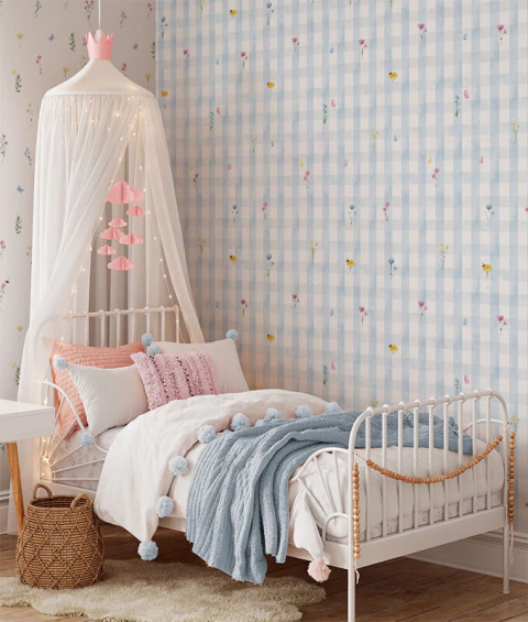 Quarto infantil feminino com papel de parede xadrez azul claro e flores aquareladas, cama branca com dossel branco decorado com luzes pisca-pisca e móbile rosa de nuvens, cobertores e almofadas em tons de rosa e azul