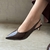 Pés femininos com sapato slingback marrom em verniz com salto baixo, ideal para compor looks elegantes e confortáveis.