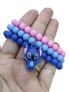 Mix de miçangas em cores azul, rosa e lilás com um pingente do personagem Stitch, segurado na mão.