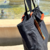 Bolso de lona negro con detalles en cuero y borlas de colores, colocado cerca de una fuente.