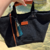 Bolso de lona negro con detalles en cuero marrón y un llavero decorativo con borlas de colores.