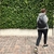 Mujer caminando con una mochila negra Siena, vestida con sudadera gris y pantalones oscuros, frente a una pared verde.