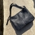 Cartera negra grande de cuero con correa regulable sobre fondo de cemento beige.