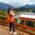 Mujer de espaldas con una tote bag color suela, disfrutando de una vista panorámica de montañas y un lago en un día nublado.