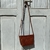 Mini bag Malta bandolera de cuero marrón con patrón de piel de cocodrilo, colgado del tirador de una puerta vintage pintada de gris claro. El diseño elegante incluye una correa larga y una forma trapezoidal.