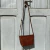 Mini bag Malta bandolera de cuero marrón con patrón de piel de cocodrilo, colgado del tirador de una puerta vintage pintada de gris claro. El diseño elegante incluye una correa larga y una forma trapezoidal.