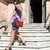 Una mujer caminando por escaleras de mármol, llevando una bandolera de cuero pequeña color roja mini bag.