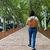 Mujer de espaldas caminando por una vereda, llevando una mochila de cuero color suela.