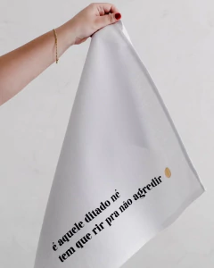 Pano de prato branco com a frase "é aquele ditado né tem que rir pra não agredir" estampada em preto.