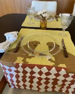 Pano de prato "Caramelos Ébrios" com estampa de cães, adornando uma mesa com pratos e copos.