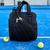 Bolso Paletero Neo Bag Bomber Negro en una cancha de pádel junto a una raqueta y pelotas.
