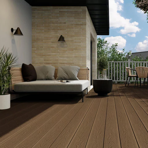 Terraza moderna con deck de PVC composite color marrón oscuro, sofá con cojines claros y mesa auxiliar negra, rodeada de plantas y cielo despejado