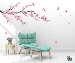 Adesivo decorativo de galho de árvore com flores de cerejeira e pássaros, em um ambiente moderno com uma poltrona verde e vaso de flores.