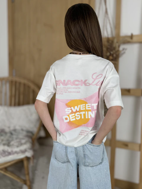 Niña de espaldas usando remera blanca de algodón modelo Destiny Over con estampa colorida en la espalda y pantalón de jean claro