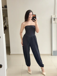 Mulher sorridente usando macacão preto tomara que caia estilo Aladim com calça ampla e punhos ajustados, posando em frente a um espelho em ambiente interno
