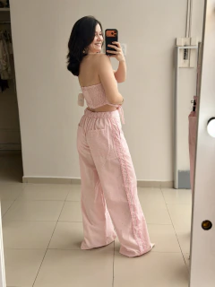 Mulher sorridente tirando selfie de costas usando conjunto rosa tomara que caia com calça larga e detalhes delicados