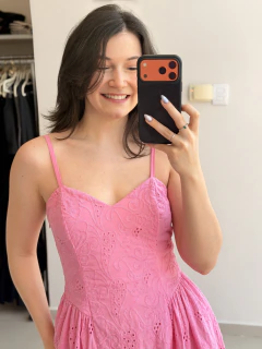 Mulher sorrindo vestindo vestido rosa laise com alças finas, tirando selfie com celular em ambiente interno