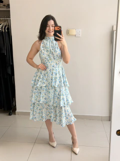 Mulher sorridente tirando selfie em espelho usando vestido babado com estampa de pequenas rosas azuis e gola alta