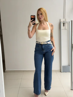Mulher loira tirando selfie em espelho vestindo top halter branco e calça jeans azul