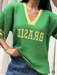 Blusa tricot verde com gola em V amarela e escrita "BRASIL" em amarelo na frente, usada por mulher com jeans