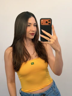 Mulher tirando selfie usando top tube amarelo com estampa da bandeira do Brasil e calça jeans azul