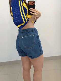 Mulher vestindo short jeans mom azul de lavagem média, visto de costas, tirando selfie em espelho com celular