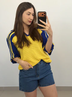 Mulher tirando selfie com smartphone vestindo short jeans mom azul e blusa amarela com detalhes azuis