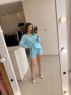 Mulher tirando selfie em espelho vestindo conjunto azul claro de camisa manga longa e short com elástico na cintura, calçando scarpin bege em ambiente interno