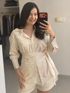 Mulher sorridente tirando selfie usando camisa listrada bege com lenço removível amarrado na cintura