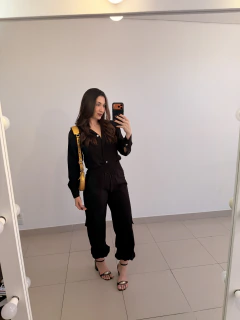 Mulher tirando selfie em espelho vestindo conjunto preto de viscose com calça e camisa de botões, sandálias pretas e bolsa amarela