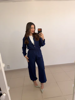 Mulher tirando selfie em espelho, vestindo conjunto feminino azul escuro com blusa de botões e calça de cintura alta com bolsos laterais, sapatos de salto alto claros