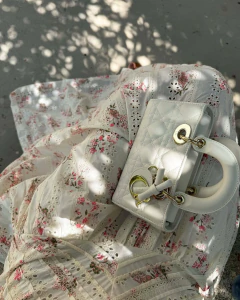 Mulher vestindo conjunto Fiorenza em algodão estampado com bordados florais e detalhes em guipir, segurando bolsa branca elegante