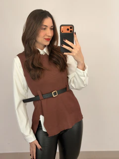 Mulher tirando selfie vestindo conjunto com camisa branca de manga longa e colete tricot marrom com cinto preto, calça preta justa