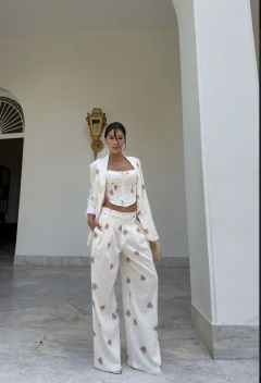 Mulher vestindo conjunto trijunto de linho branco com estampa floral rosa, composto por blazer, corset e calça de perna larga