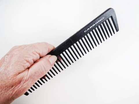 Pente de cabelo preto fosco feito de carbono e plástico, com dentes médios e finos, exibindo um design elegante e profissional.